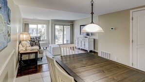 A dining area with a wooden table, chairs, a lamp, and a television on a cabinet. - Beautiful condo with pool, tennis, balcony, central AC, & washer dryer (Hilton Head)