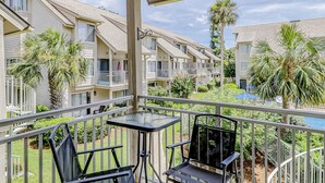A balcony with a table and chairs, overlooking a pool and adjacent buildings. - Beautiful condo with pool, tennis, balcony, central AC, & washer dryer (Hilton Head)
