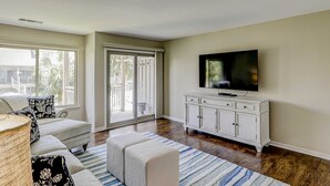 A living room with a sofa, ottoman, TV, and white cabinet. - Beautiful condo with pool, tennis, balcony, central AC, & washer dryer (Hilton Head)