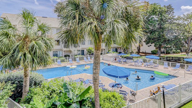 A pool area with multiple swimming pools, lounge chairs, and palm trees. - Beautiful condo with pool, tennis, balcony, central AC, & washer dryer (Hilton Head)
