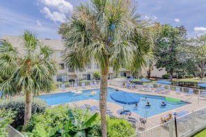 A pool area with multiple swimming pools, lounge chairs, and palm trees. - Beautiful condo with pool, tennis, balcony, central AC, & washer dryer (Hilton Head)