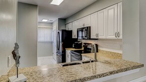 A kitchen with white cabinets, a granite countertop, a microwave, a refrigerator, and a sink. - Beautiful condo with pool, tennis, balcony, central AC, & washer dryer (Hilton Head)