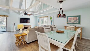 A spacious living area with a glass-top dining table, white chairs, a ceiling fan, and a television. - Gated community home with lagoon & pools Near Beaches & Dog Friendly (Hilton Head)
