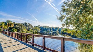 A wooden boardwalk with a metal railing overlooking a calm lake, surrounded by dense greenery. - Gated community home with lagoon & pools Near Beaches & Dog Friendly (Hilton Head)