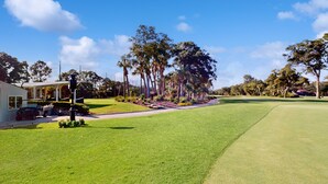 A golf course with a well-maintained lawn, a house with a porch, and tall trees in the background. - Gated community home with lagoon & pools Near Beaches & Dog Friendly (Hilton Head)