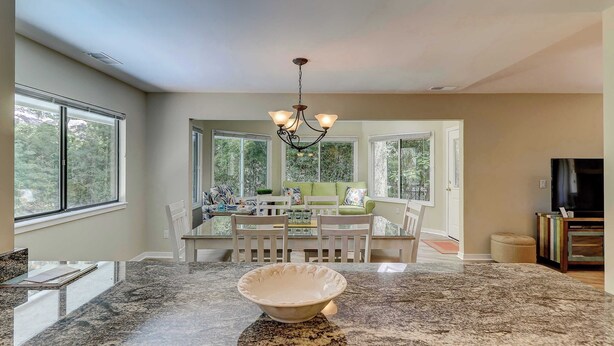 A spacious kitchen with granite countertops, a dining area with white chairs, and a chandelier. - Cozy dog-friendly home with free WiFi & private pool for a relaxing stay (Hilton Head)