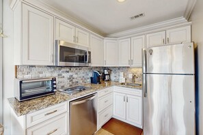 A kitchen with white cabinets, stainless steel appliances, a toaster oven, and a coffee maker. - Top Floor Condo w/ Ocean Views, Pool, Balcony & WIFI - Walk to Beach (Hilton Head)