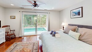 Ein Schlafzimmer mit einem Bett, einem Deckenventilator, einem Fenster mit Blick auf einen Pool und einem gerahmten Bild an der Wand.