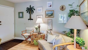 A room with a wooden floor, a sofa, a dining table with chairs, and various wall decorations. - Terrific island escape with pool, furnished patio, fast WiFi & beach nearby (Hilton Head)