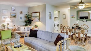 A living room with a sofa, armchairs, a coffee table, a dining area with chairs, a ceiling fan, and a washing machine in the background. - Terrific island escape with pool, furnished patio, fast WiFi & beach nearby (Hilton Head)