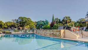 Una piscina con pared de piedra y barandilla metálica, rodeada de árboles y una escalera.