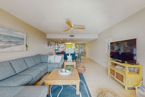 A living room with a sofa, a coffee table, a TV stand, and a ceiling fan. - Beachfront getaway with WiFi, pools, hot tub, gym, washer dryer, & central AC (Hilton Head)