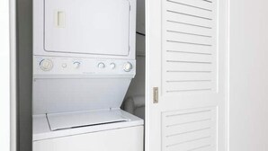 Une buanderie blanche avec un sèche-linge et une porte dotée de panneaux à persiennes horizontales.