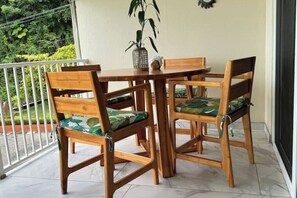 A wooden table and chairs with green patterned cushions on a balcony with a white railing and a potted plant. - Terrace with private access and view of Playa Blanca (Puntarenas)