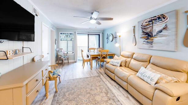 A living room with a beige sofa, a TV, a ceiling fan, and a dining area with a table and chairs. - Hilton Head Resort Villa with AC, pool, hot tub, tennis - near beach & golf (Hilton Head)