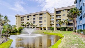 A multi-story hotel with a central courtyard featuring a fountain, surrounded by greenery and palm trees. - Hilton Head Resort Villa with AC, pool, hot tub, tennis - near beach & golf (Hilton Head)