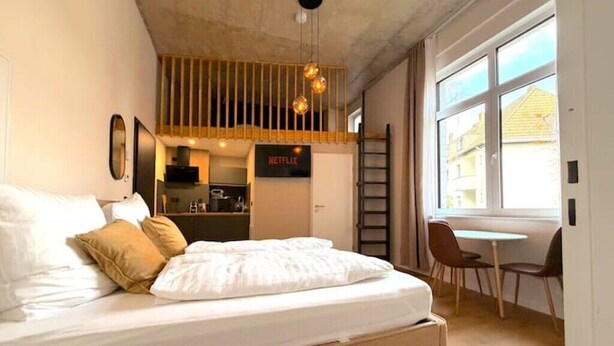 A bedroom with a bed, a TV, a kitchenette, and a window.