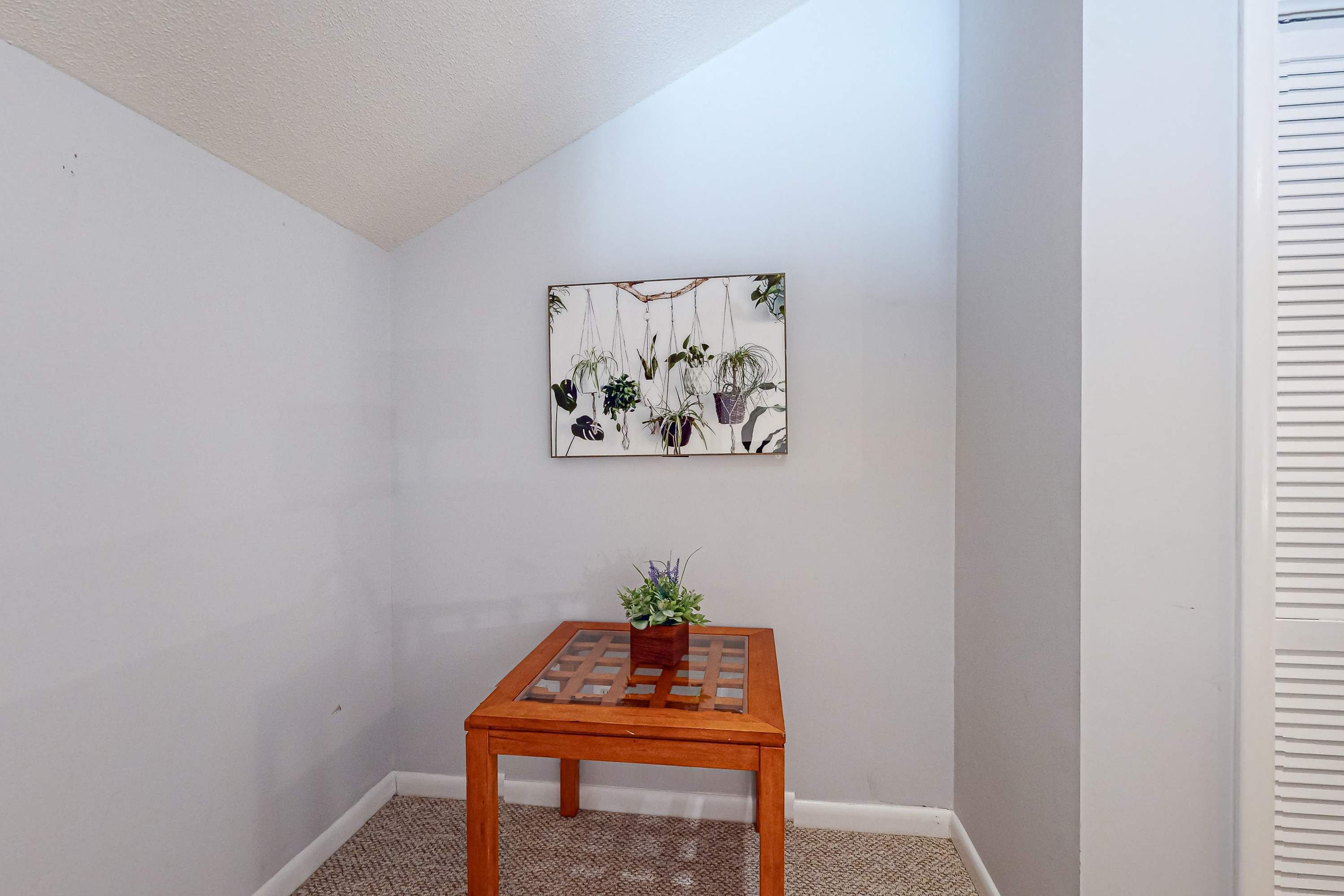A corner room with a wooden table, a potted plant, and a wall-mounted artwork.