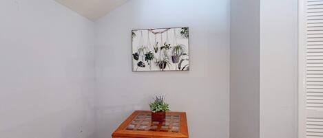A corner room with a wooden table, a potted plant, and a wall-mounted artwork.