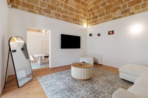 Een moderne woonkamer met een bakstenen plafond, een flatscreen televisie, een rond poef en een vloerkleed met patroon.