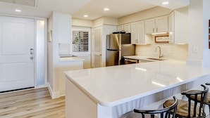 A modern kitchen with a large island, white cabinetry, and a stainless steel refrigerator. - Beachfront escape with pools, hot tub, WiFi, washer/dryer, & central AC (Hilton Head)