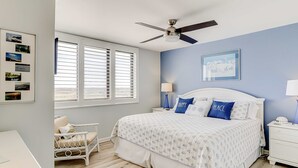 A bedroom with a bed, a chair, a nightstand, a ceiling fan, and a window with blinds. - Beachfront escape with pools, hot tub, WiFi, washer/dryer, & central AC (Hilton Head)