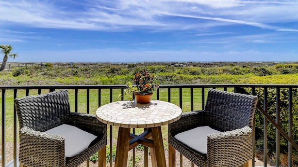 A balcony with wicker chairs and a round table, overlooking a grassy landscape and a distant view. - Beachfront escape with pools, hot tub, WiFi, washer/dryer, & central AC (Hilton Head)