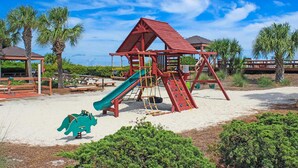 Un terrain de jeux avec un toboggan, une zone d’escalade et un petit jouet dinosaure vert.