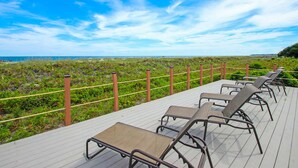 Une terrasse avec des chaises longues donnant sur une plage, séparée de celle-ci par une clôture et agrémentée de verdure.