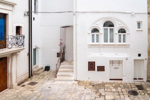 A narrow street with a white building featuring a staircase, a wooden door, and a metal gate. - Suite apartment with jacuzzi (Gioia del Colle)