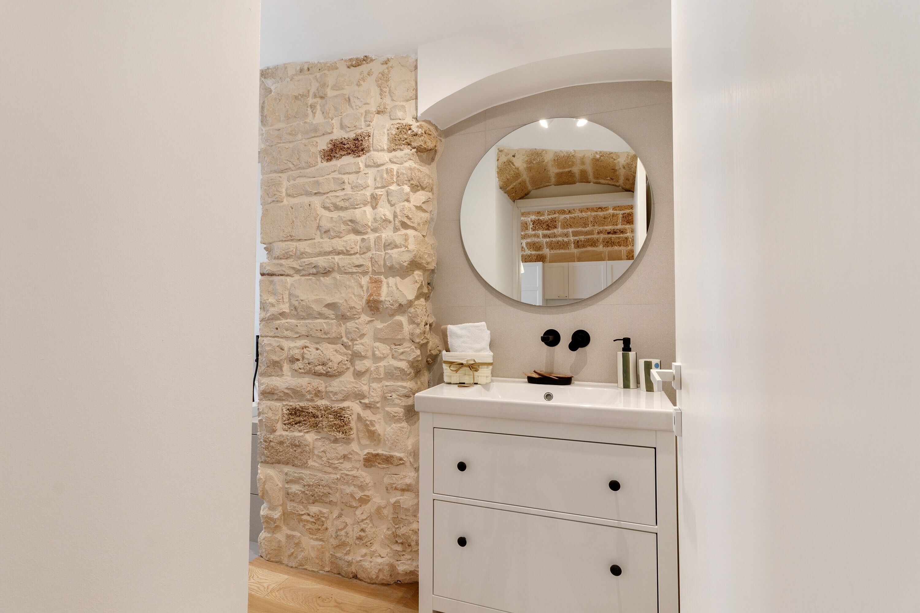 A bathroom with a stone wall, a round mirror, a white sink, and two drawers.