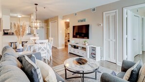 A modern living room with a sofa, coffee table, TV, and dining area. - Charming condo with shared pools and hot tub, high-speed WiFi, and central AC (Hilton Head)