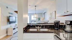 A modern kitchen with a double sink, a coffee maker, and a television mounted on the wall. - Charming condo with shared pools and hot tub, high-speed WiFi, and central AC (Hilton Head)