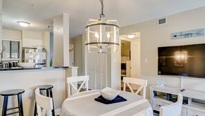 A modern kitchen with white cabinetry, a central island, and a dining area with a round table and bar stools. - Charming condo with shared pools and hot tub, high-speed WiFi, and central AC (Hilton Head)