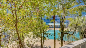 A pool area with trees, a clear sky, and a building with blue windows in the background. - Charming condo with shared pools and hot tub, high-speed WiFi, and central AC (Hilton Head)