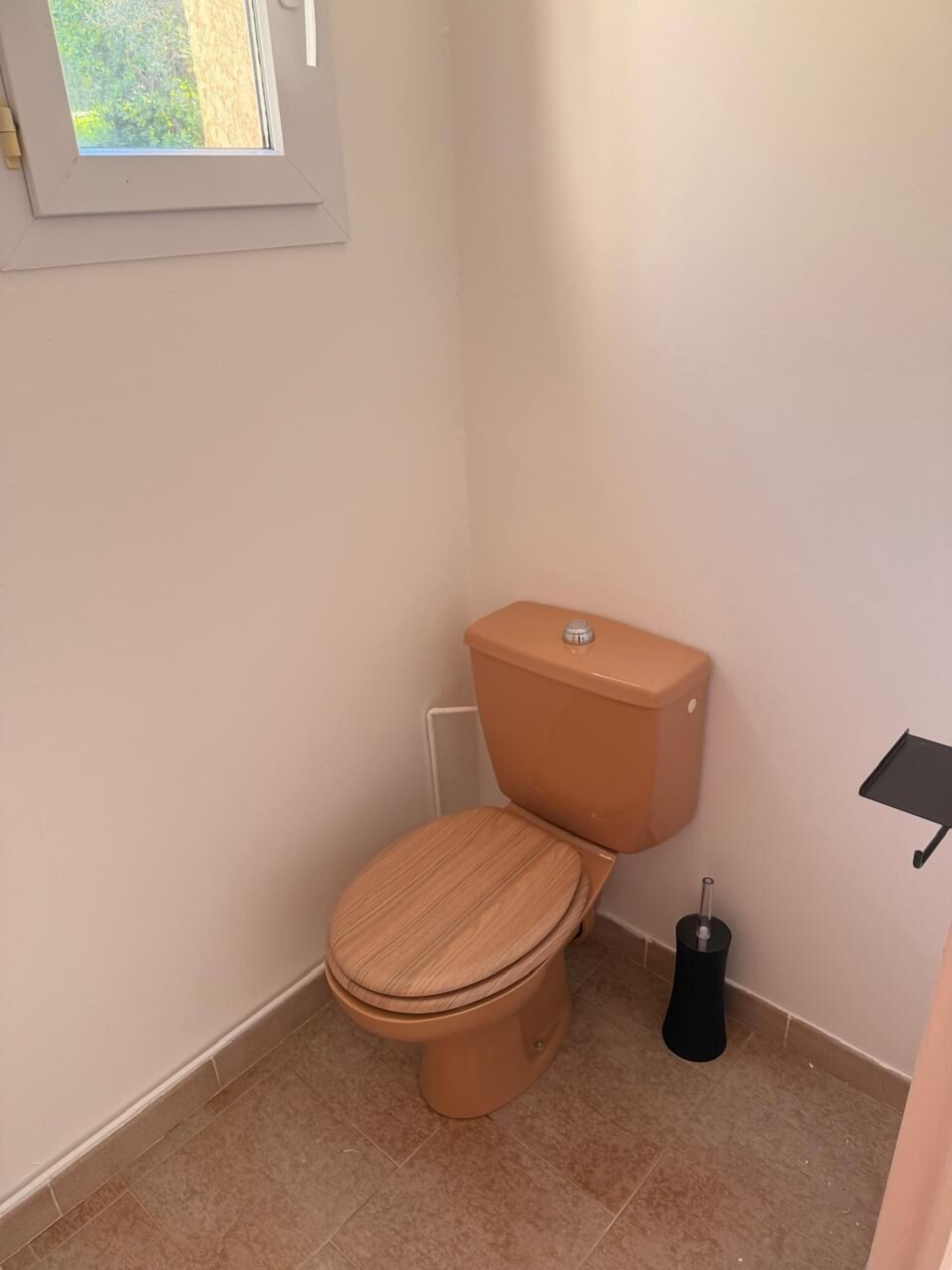 Un baño pequeño con inodoro, una ventana y un cubo de basura negro.