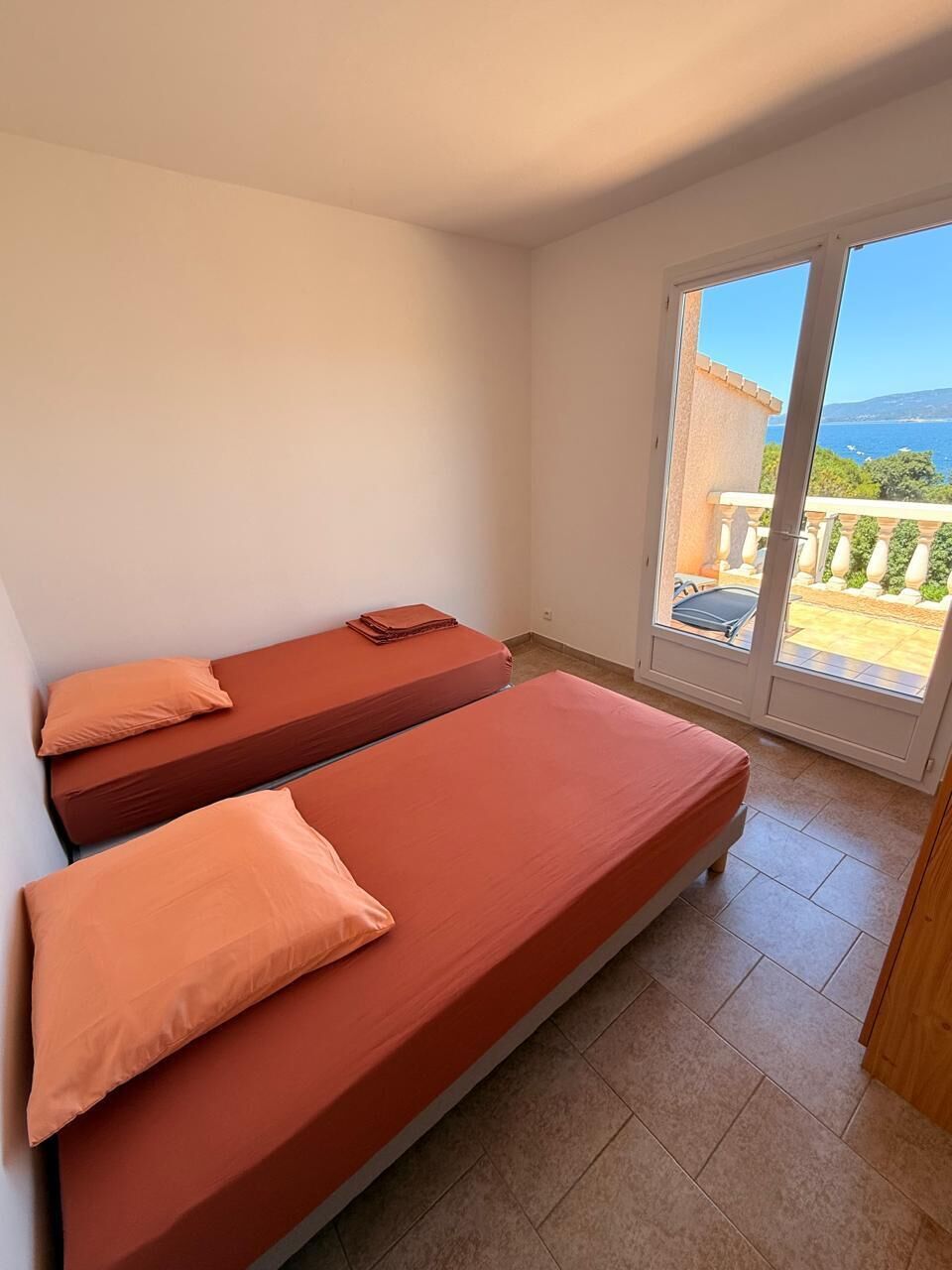 Een kamer met twee bedden, een schuifglasdeur naar een balkon en uitzicht op zee.