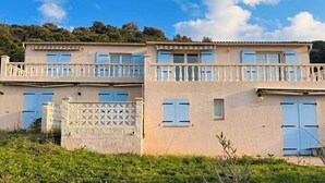 A two-story building with balconies, a lattice fence, and a grassy foreground. - F3 in very quiet villa, large terrace with sea view, beach 5 minutes away on foot (Calcatoggio)