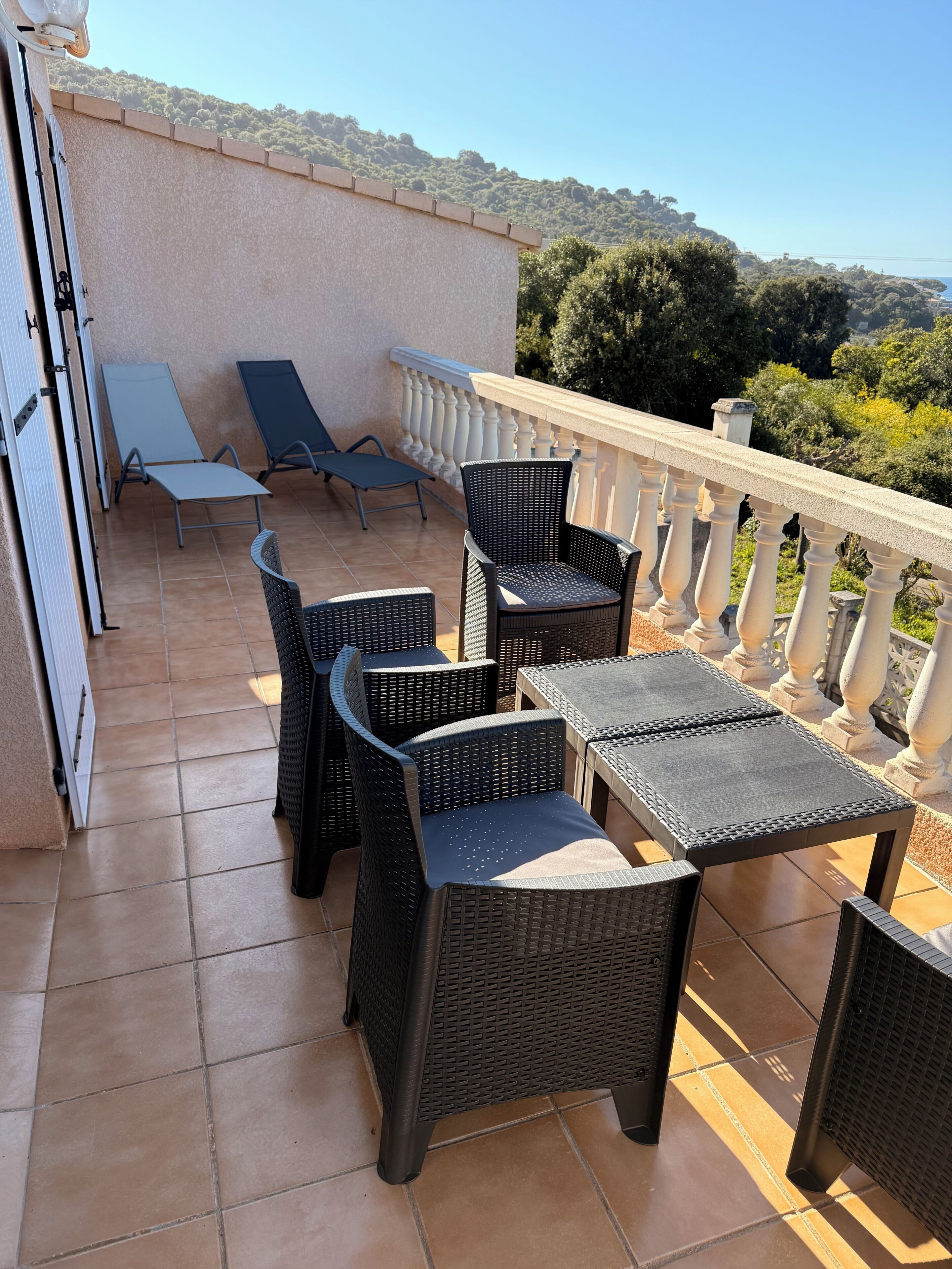 Eine Terrasse mit Korbmöbeln, einem weißen Geländer und Blick auf eine hügelige Landschaft.