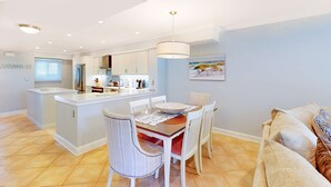 Een moderne keuken met witte kasten, een centraal eiland en een eethoek met een tafel en stoelen.