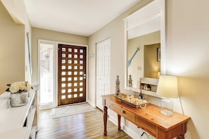 Un pasillo con una puerta de madera, una puerta blanca, una consola de madera con una lámpara y un espejo.