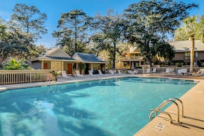 Una piscina con sillas de descanso, un área de estar techada y un edificio con un porche.