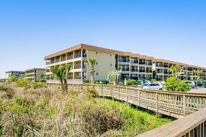 A multi-story hotel with balconies, a parking area, and a wooden boardwalk. - 3rd floor condo with private balcony, AC, Washer and Dryer, on site pools, hot tub & tennis (Hilton Head)