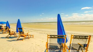 Cadeiras de praia com guarda-sóis azuis numa praia arenosa.