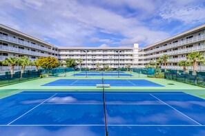 Ein Tennisplatz mit Netz, umgeben von einem mehrstöckigen Gebäude mit Balkonen.