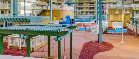 A multi-level indoor pool area with various water features, a children's play area, and a view of the surrounding building structure.