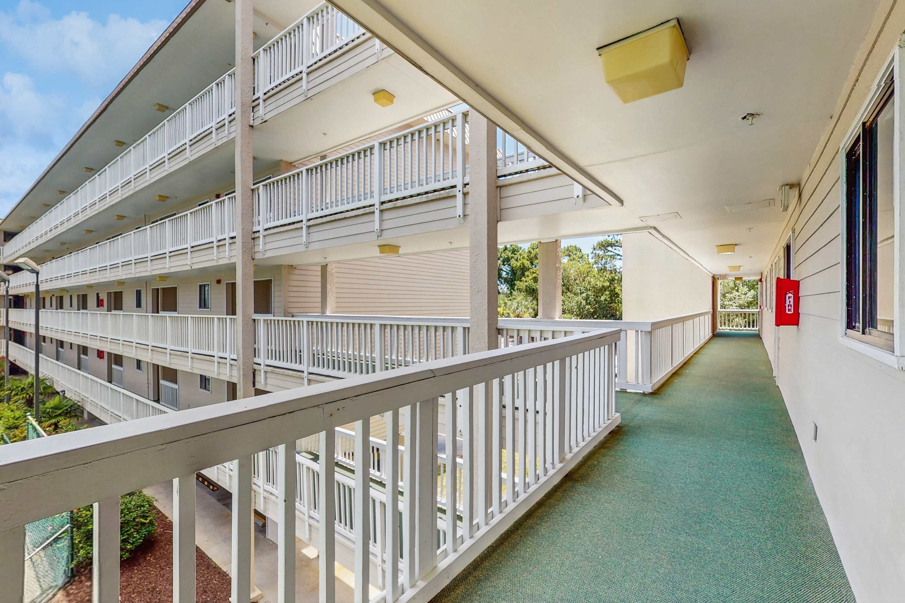 A multi-story hotel corridor with balconies, a green carpeted floor, and a red emergency phone.