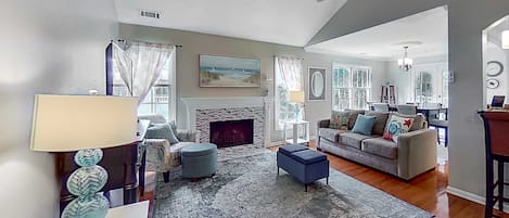 A spacious living room with a fireplace, a ceiling fan, and a large window.