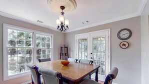 Ein Esszimmer mit Holztisch, Stühlen, einer Chandelier und großen Fenstern.