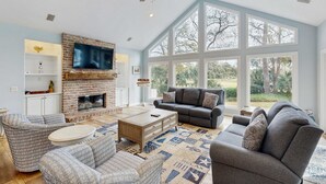 A spacious living room with a brick fireplace, large windows, and comfortable seating. - Beautiful half acre estate home with private hot tub and passes to the shared pool (Hilton Head)